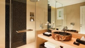 foto badezimmer mit viel glas und spiegeln und einem aus einem grossen stein geschliffenen waschbecken dazu viele handtücher und pflegeprodukte im luxuriösen hochklassigen exklusiven designer hotel santa marina auf mykonos in griechenland europa